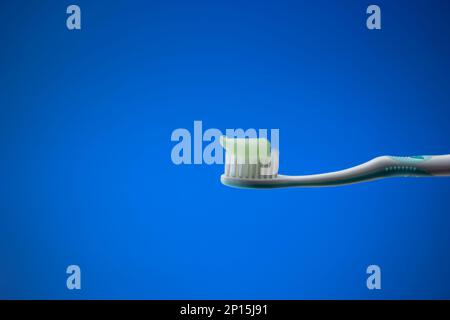 White plastic toothbrush with light blue toothpaste. Close up studio shot, isolated on blue background, no people. Stock Photo