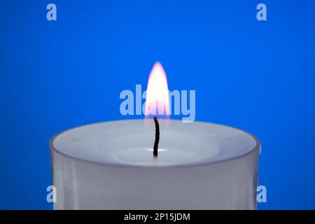 Single small white candle burning. Close up studio shot, isolated on blue background. Stock Photo
