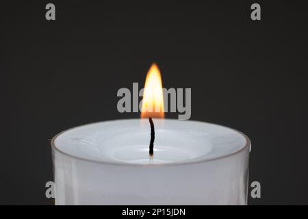 Single small white candle burning. Close up studio shot, isolated on dark background. Stock Photo