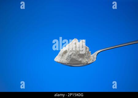 White cooking flour in a small spoon. Close up studio shot, isolated on blue background. Stock Photo
