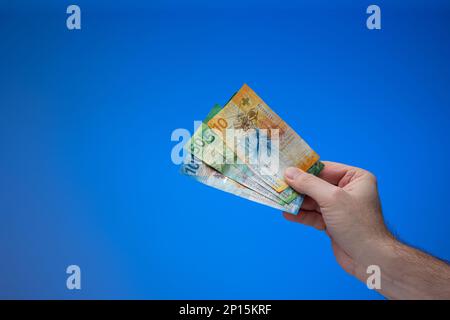 Swiss franc banknotes held by male hand. Close up studio shot, isolated on blue background. Stock Photo
