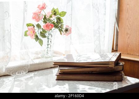 vintage brown photo albums stand on the table in a stack near the window with flowers on the windowsill Stock Photo
