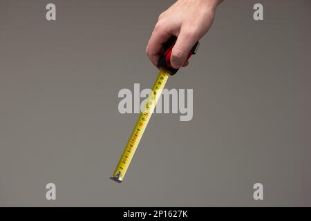 Caucasian male hand holding a measuring tape ruler isolated on gray background. Stock Photo