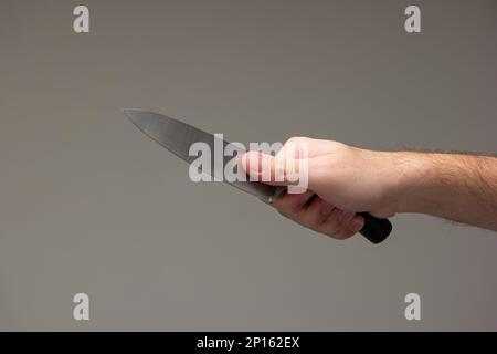 Caucasian male hand holding a large kitchen knife isolated on gray background. Stock Photo