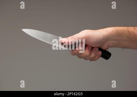 Caucasian male hand holding a large kitchen knife isolated on gray background. Stock Photo