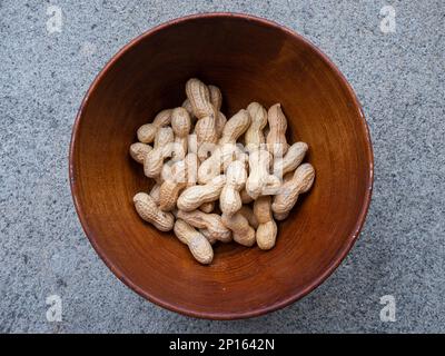 Group of unpeeled peanuts in a brown wooden bowl top view close up shot. Stock Photo
