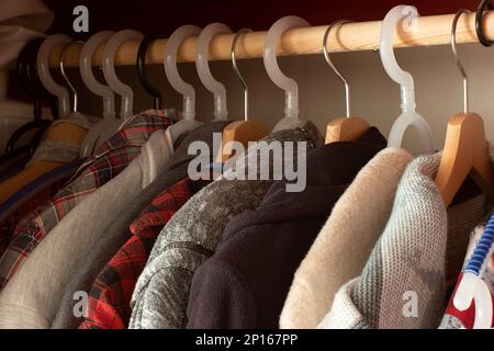 Row of various mix colored clothing items on hangers inside home closet red wooden cupboard. Stock Photo