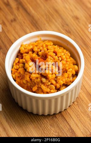 Home cooked bulgur pilaf in a white ceramic portion cup on a kitchen wooden board top view. Stock Photo