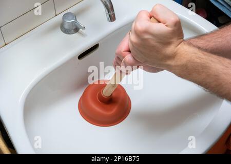 Caucasian male hand holding a plunger unclogging a bathroom sink. Stock Photo