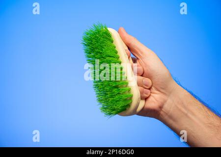 Caucasian male hand holding a plastic cleaning wire scrub brush studio shot isolated on blue background. Stock Photo