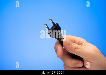 Caucasian male hand holding a black power cord plug studio shot isolated on blue background. Stock Photo