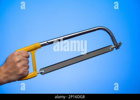 Caucasian male hand holding a hand saw with yellow plastic handle studio shot isolated on blue background. Stock Photo