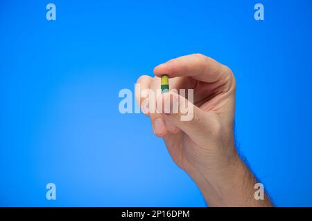 Yellow and green capsule medical pill held between fingers by Caucasian male hand isolate on blue background studio shot Stock Photo