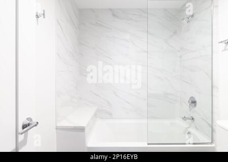 A shower with white marble tile and glass walls, a marble hexagon tiled floor, bench seat, and chrome showerhead. Stock Photo