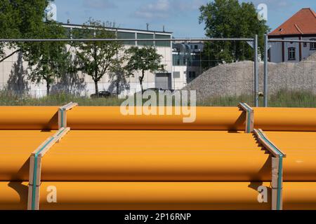 Plastic orange pipes lying along a metal lattice fence. Construction site in the background. Stock Photo