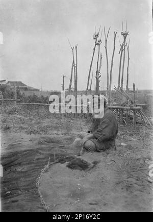 Seated Ainu man working on fishing nets, 1908. Stock Photo