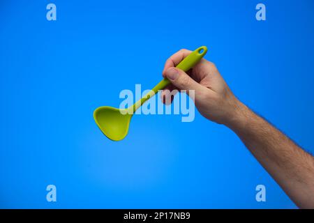 Caucasian male hand holding silicon serving ladle isolated on blue background. Stock Photo