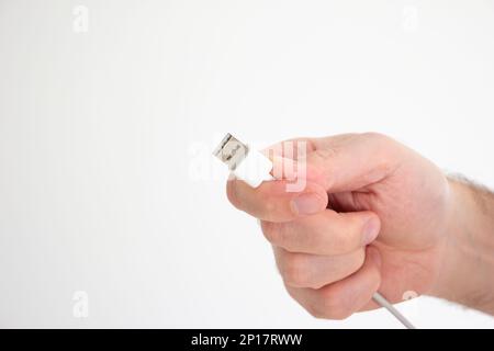 USB cable ad connector held in hand by Caucasian male hand isolated on white background. Stock Photo