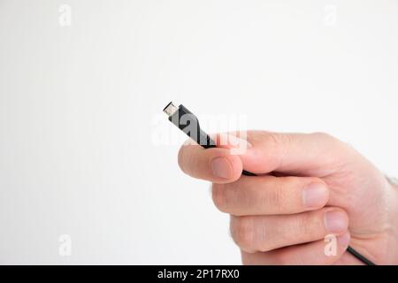 USB cable ad connector held in hand by Caucasian male hand isolated on white background. Stock Photo