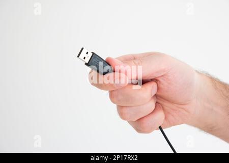 USB cable ad connector held in hand by Caucasian male hand isolated on white background. Stock Photo