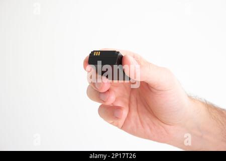 Black square format rechargeable battery held in hand by Caucasian male hand isolated on white. Stock Photo