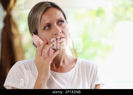 Thoughtful female speaking on smartphone at home Stock Photo
