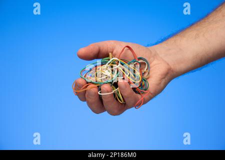 Pile of colorful rubber bands held in hand by Caucasian male hand isolated on blue. Stock Photo