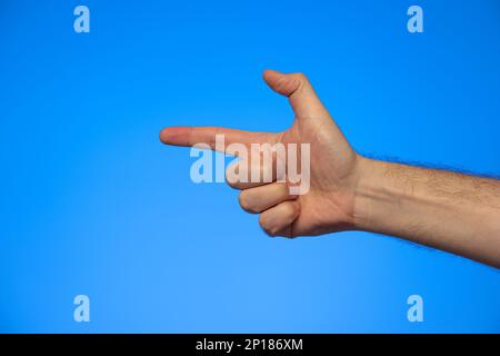 Caucasian male hand making a fake pistol gesture studio shot isolated on blue. Stock Photo