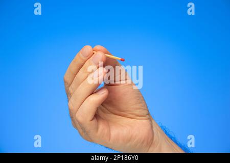 New unlit matchstick held in hand by Caucasian male hand studio shot isolated on blue. Stock Photo