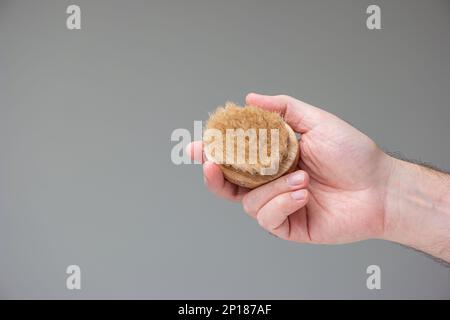 Wooden handle fruit and vegetable scrubbing brush held in hand by Caucasian male hand isolated on gray background. Stock Photo