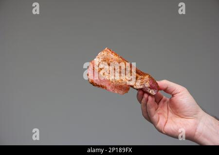 Raw seasoned sliced pork rib held by Caucasian male hand studio shot isolated on gray background. Stock Photo