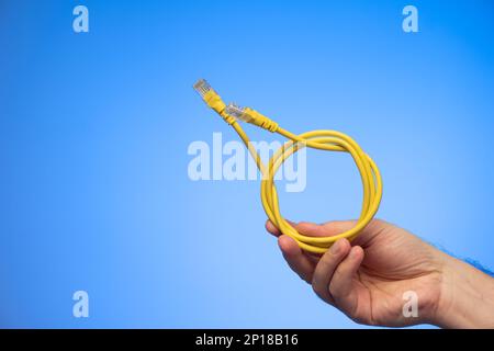 Blue folded Ethernet cable held in hand by Caucasian male hand studio shot isolated on blue background. Stock Photo