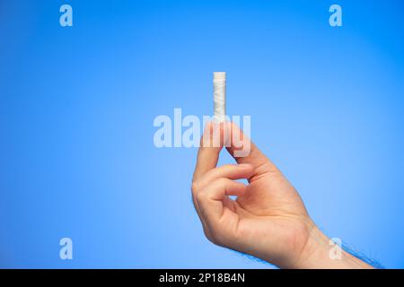 Small reel of white sewing thread held in hand by Caucasian male hand studio shot isolated on blue background. Stock Photo