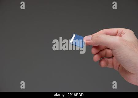 Small plastic SD memory card held in hand by Caucasian male hand studio shot isolated on gray background. Stock Photo
