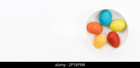 Easter eggs lie in a bowl on a white background with copy space. Easter banner in a minimalistic style. Traditional Easter eggs painted by kids in a w Stock Photo