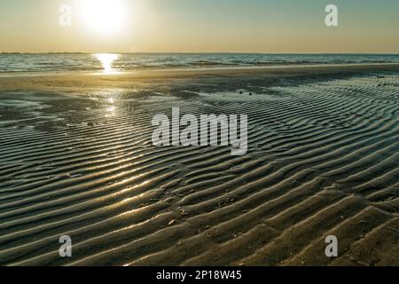 Bright sunlight reflecting across the rippled beach during setting with the ocean in the background Stock Photo