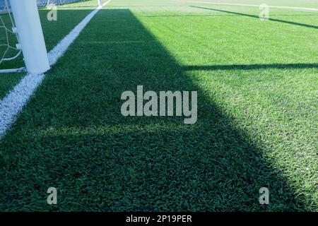 Artificial turf on football soccer field. Part of soccer goal and green synthetic grass on sport ground with shadow from goal net Stock Photo