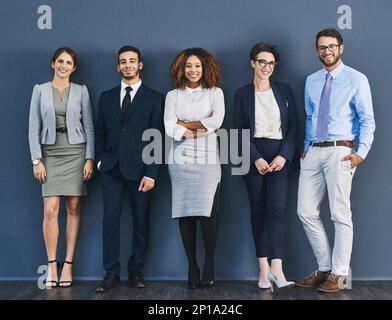 Surrounded by business minded individuals. Studio shot of a group of businesspeople standing in line against a gray background. Stock Photo