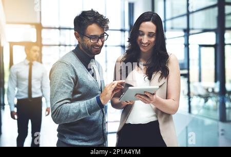 Working with twice the expertise. Shot of two businesspeople working on a digital tablet in a busy office. Stock Photo
