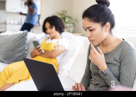 Happy diverse friends sitting on sofa, using electronic devices Stock Photo