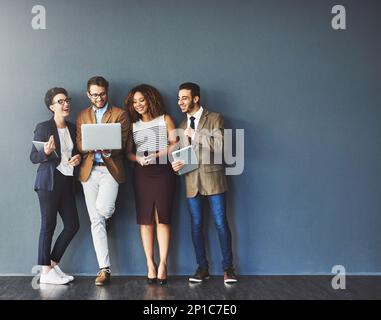 The connected team is an efficient team. Studio shot of a group of businesspeople using wireless technology together while standing in line against a Stock Photo