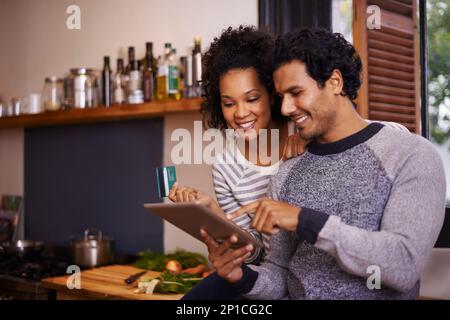 Lets download this recipe. Shot of a young couple using their tablet together while they get ready to prepare a meal. Stock Photo