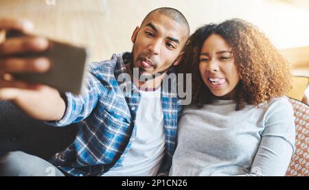 Truly, madly, crazy in love. Shot of a happy young couple taking selfies together at home. Stock Photo