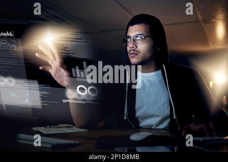 Hacking is a skill that comes second-nature to him. Shot of a young hacker cracking a computer code in the dark. Stock Photo