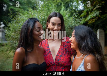 Three female friends of different ethnic backgrounds laugh together in a public park. Stock Photo