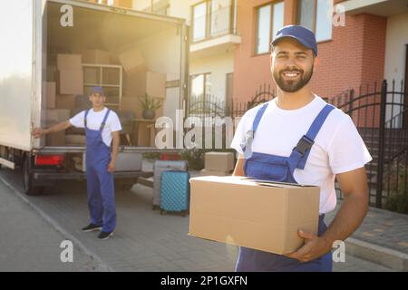 Workers unloading boxes from van outdoors. Moving service Stock Photo