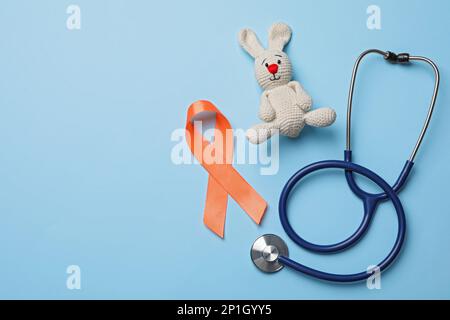 Orange ribbon, toy bunny and stethoscope on light blue background, flat lay with space for text. Multiple sclerosis awareness Stock Photo