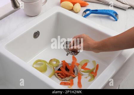 Woman putting vegetable scraps in garbage disposal at home, closeup Stock Photo