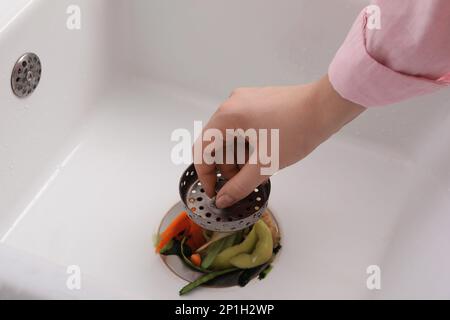 Woman putting vegetable scraps in garbage disposal at home, closeup Stock Photo