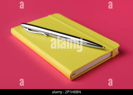 New stylish planner with hard cover and pen on pink background, closeup Stock Photo